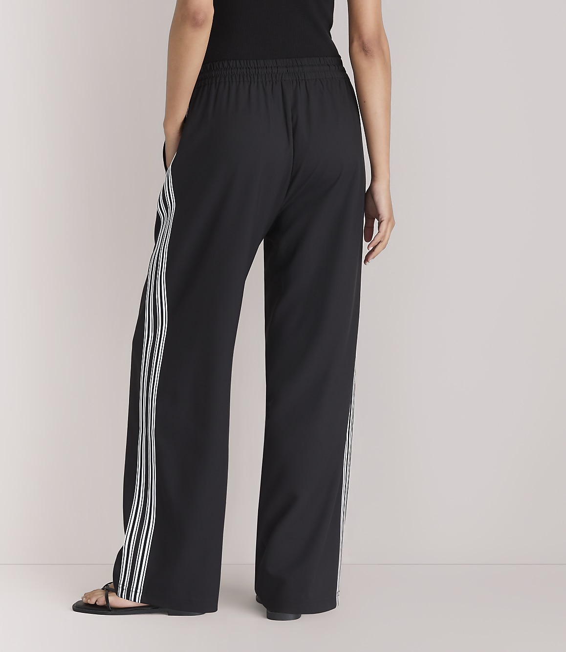 A person wearing black wide-leg pants with white stripes stands against a plain white background.