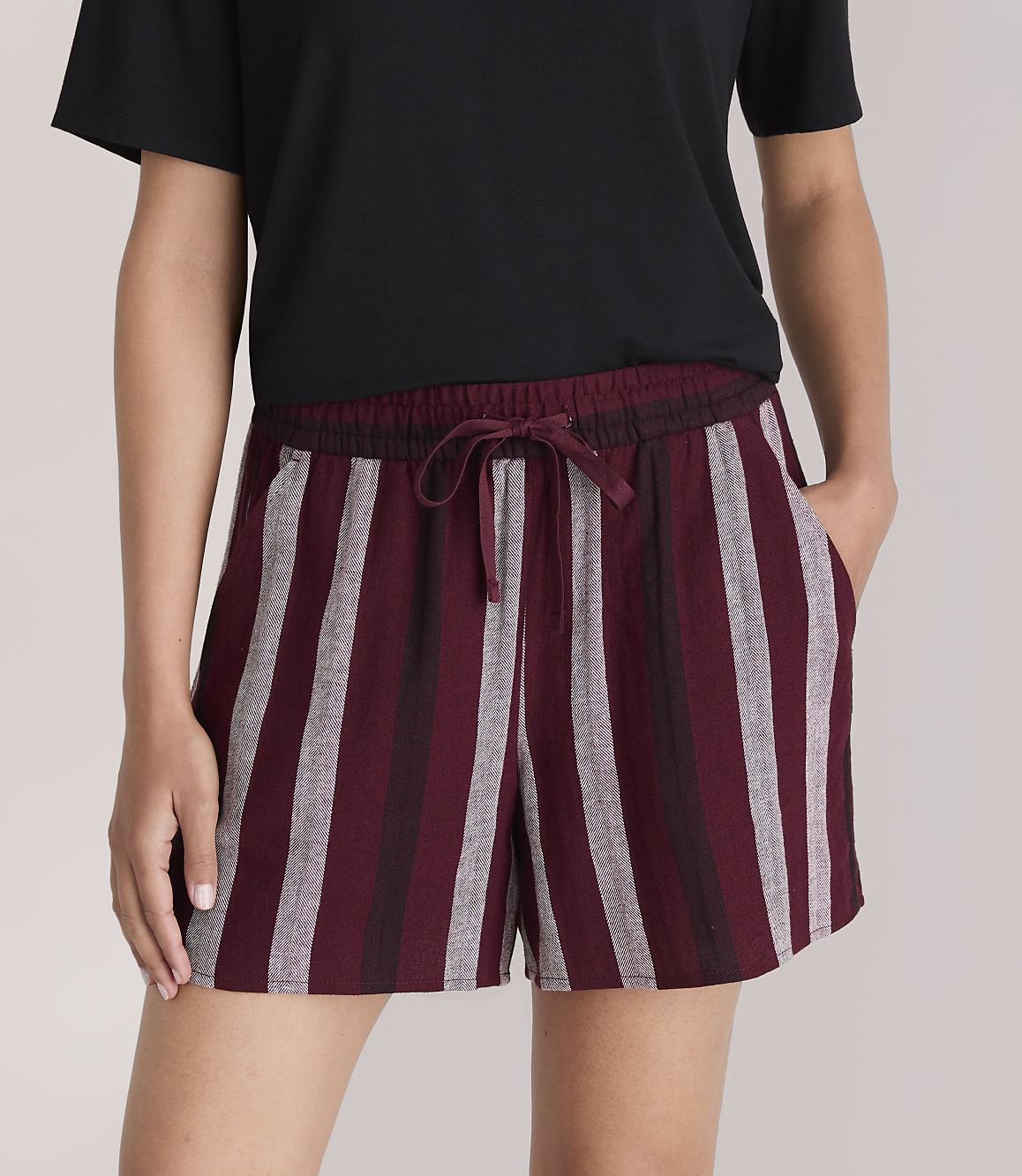 A person in a black t-shirt and striped burgundy shorts stands against a plain white background.