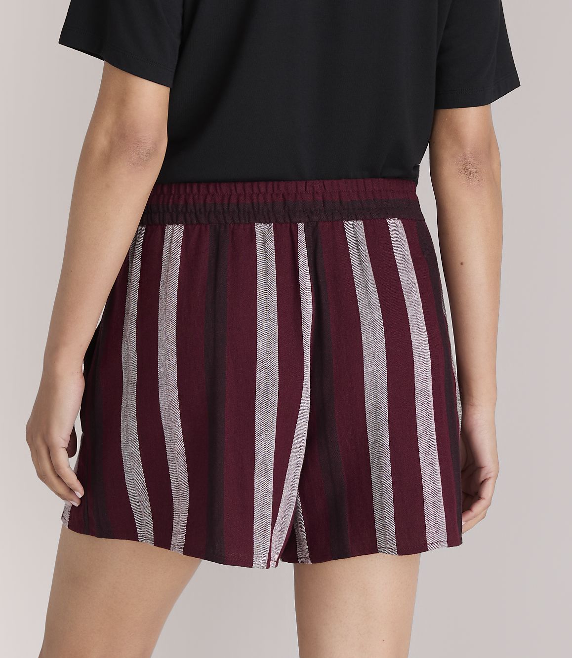 A person wearing striped burgundy and gray shorts stands against a plain gray background.