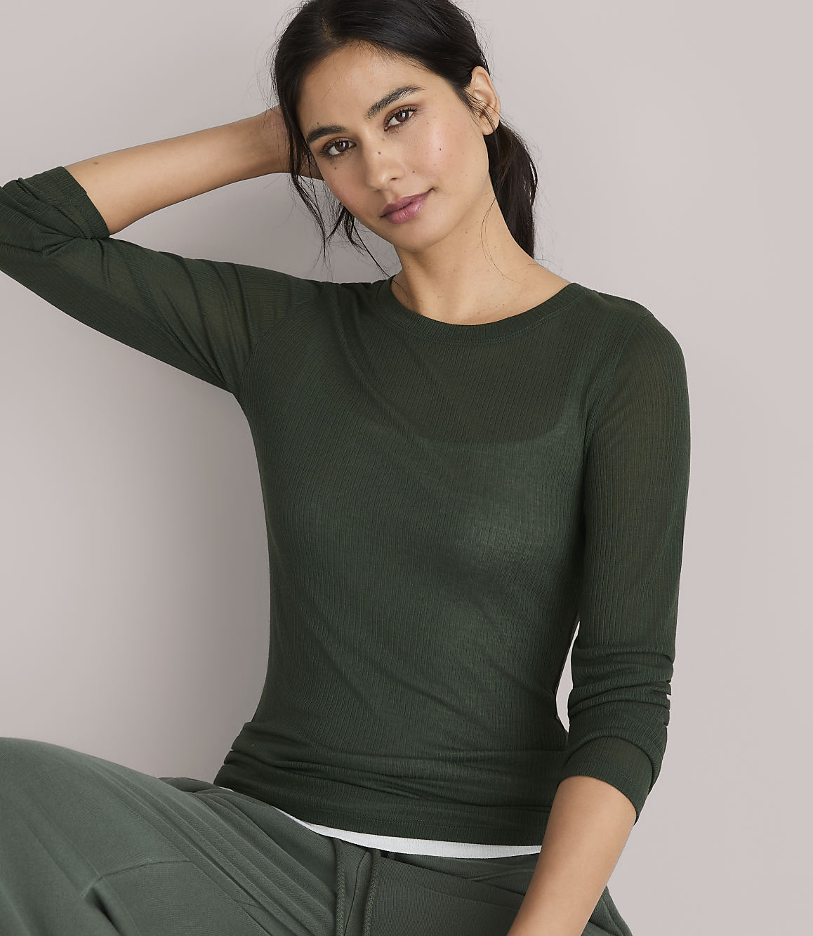 A woman in a green sweater and pants stands against a plain gray background.