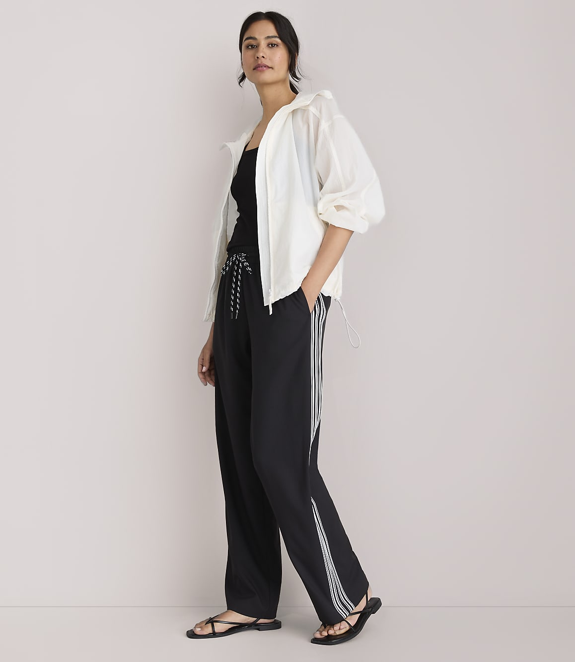 A woman in a white jacket and black athletic pants stands against a plain white background.