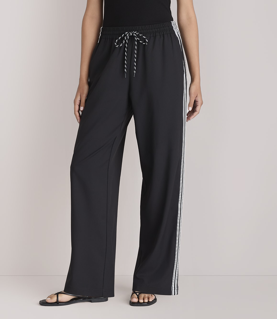 A person stands in black wide-leg pants with white stripes down the sides, against a plain white background.
