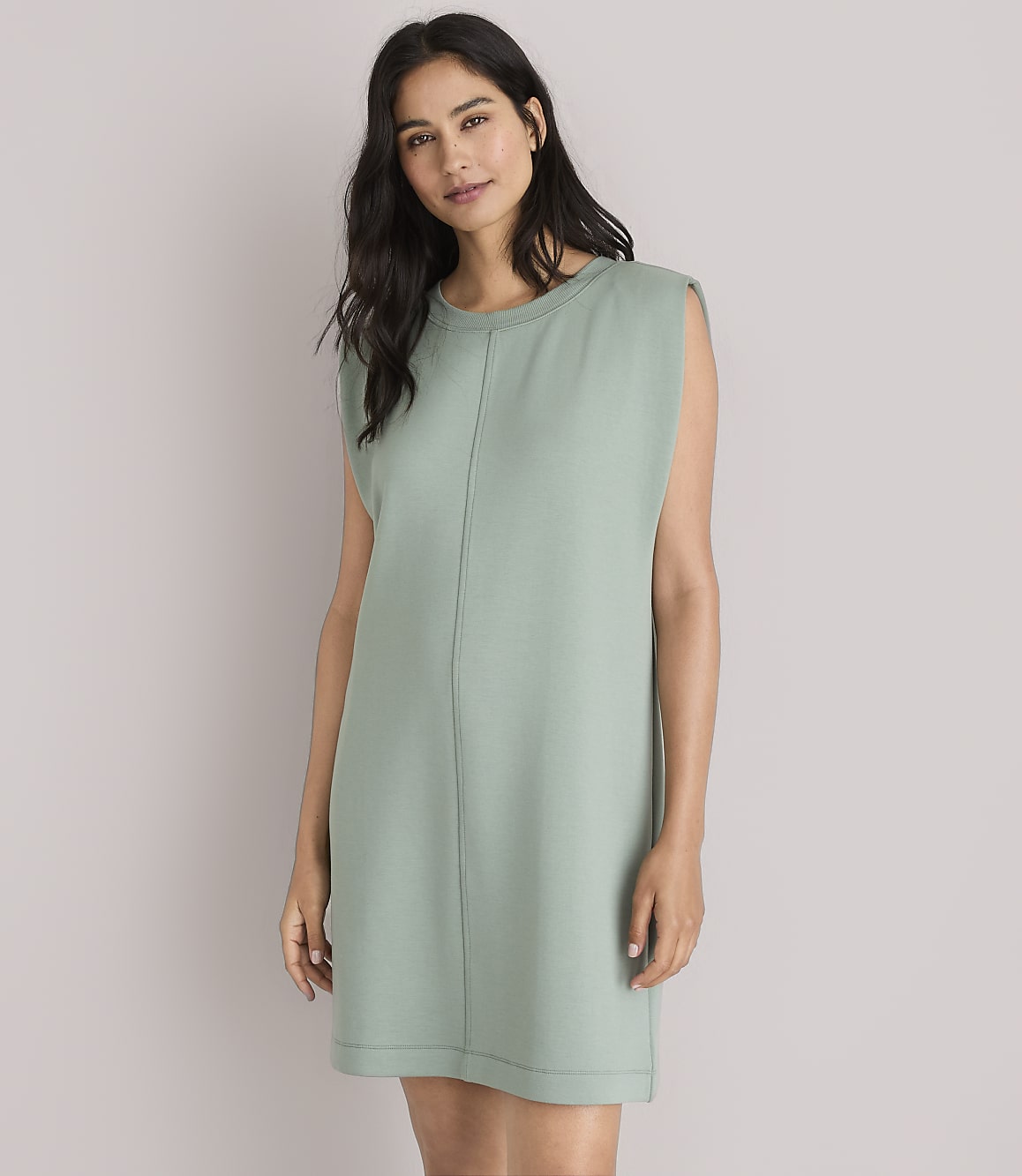 A woman in a green dress and white sandals stands against a plain white background with a striped sweater tied around her waist.