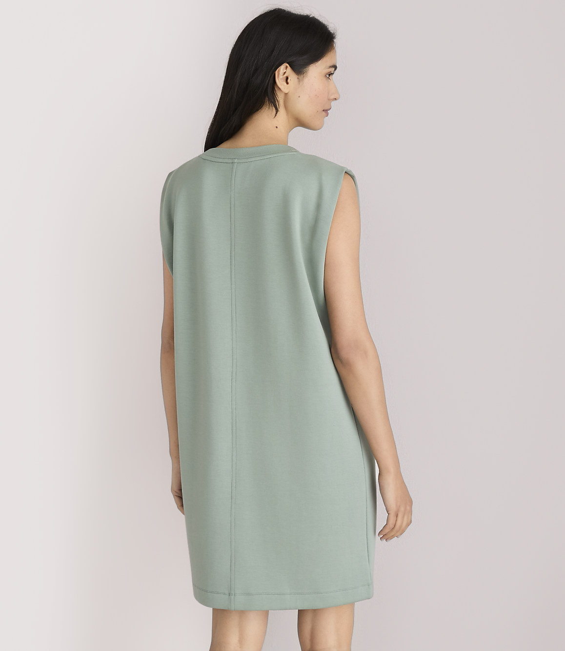 A woman in a light green sleeveless dress stands against a plain white background.
