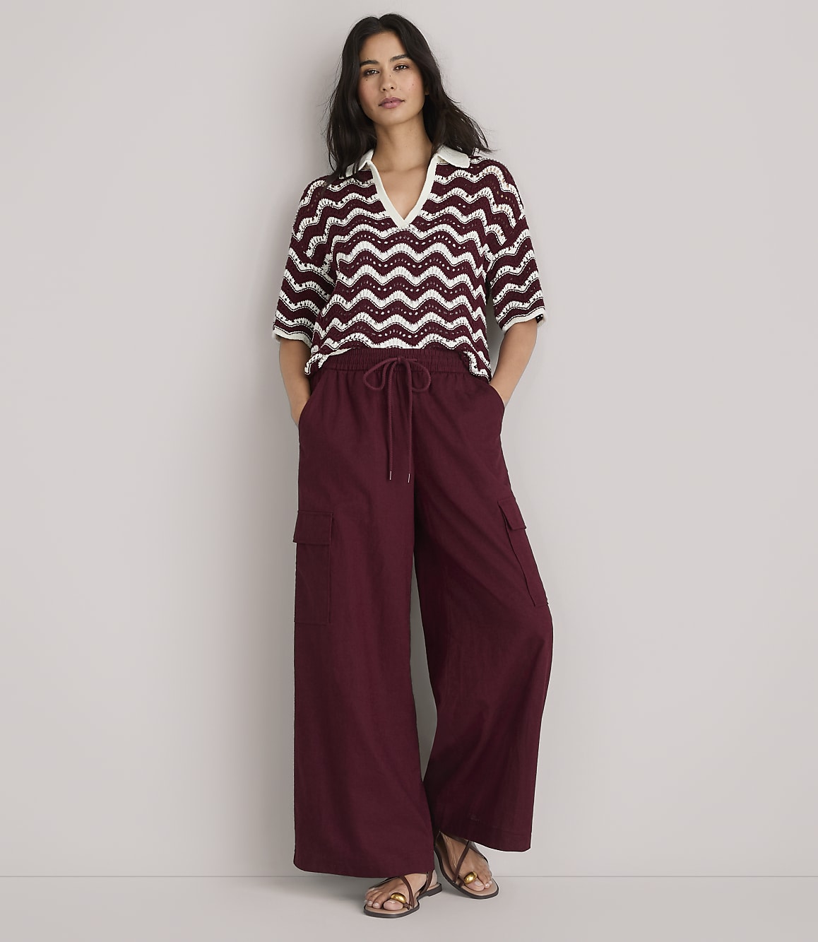 A woman in a burgundy and white chevron-patterned knit polo shirt and burgundy pants stands against a plain white background.