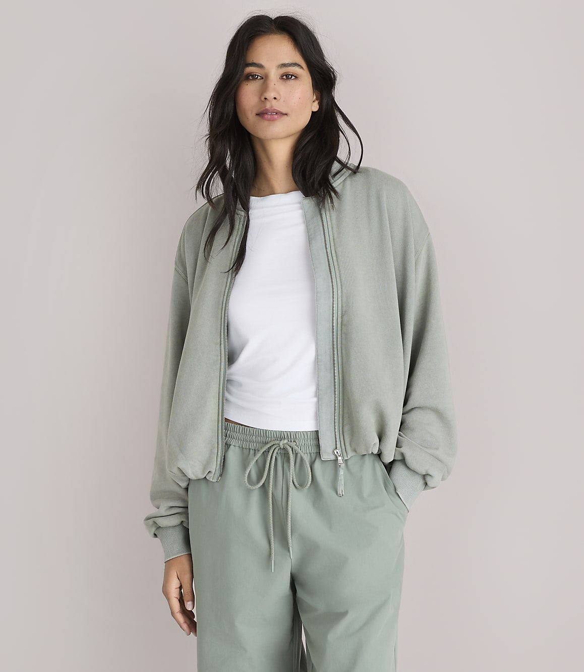 A woman in a light green bomber jacket and matching pants stands against a plain white background.