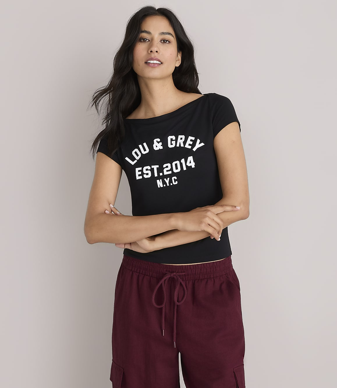 A woman in a black "LOU & GREY EST. 2014 N.Y.C." t-shirt and maroon cargo pants stands against a plain white background.