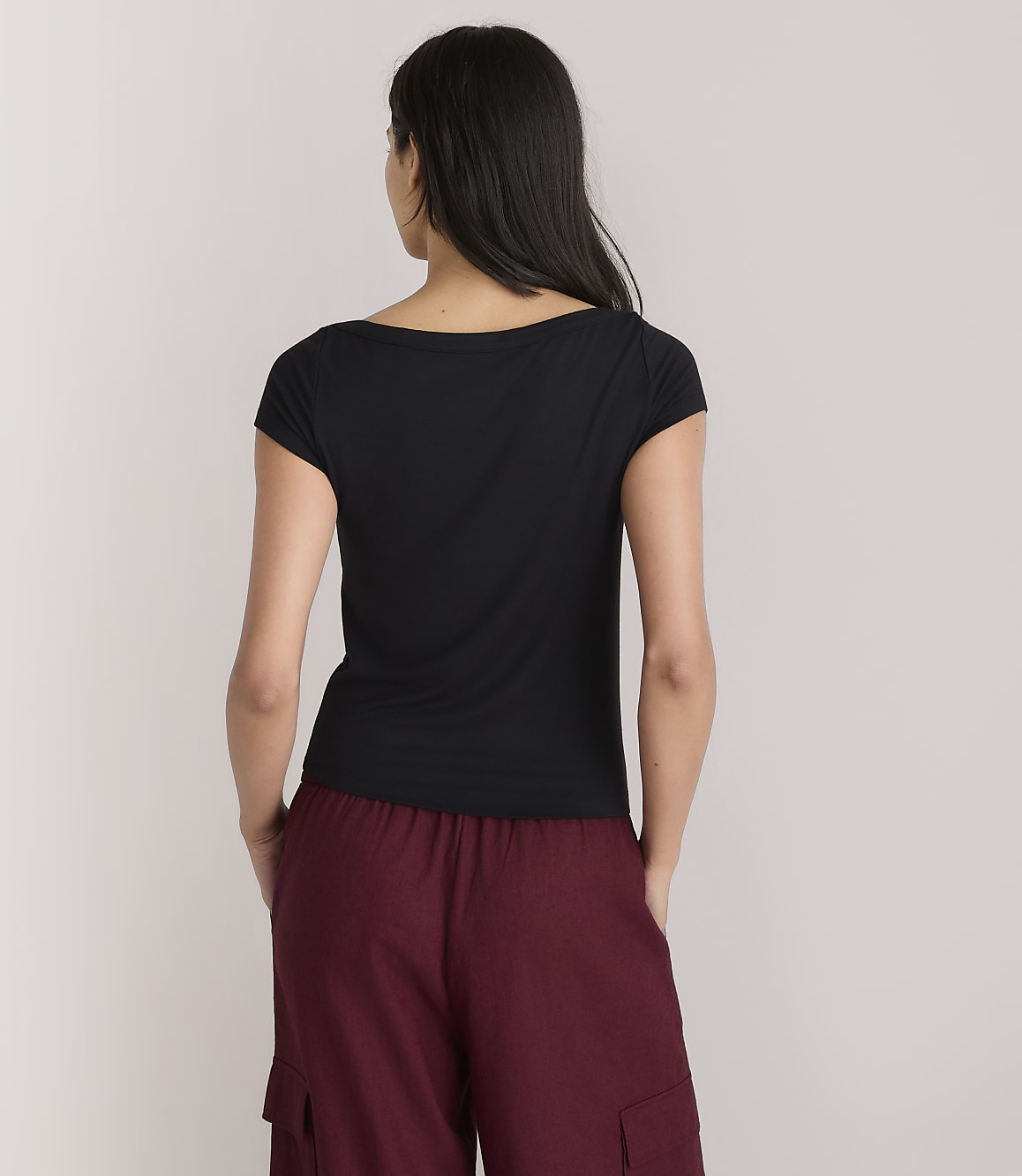 A woman in a black t-shirt and maroon pants stands against a plain white background.