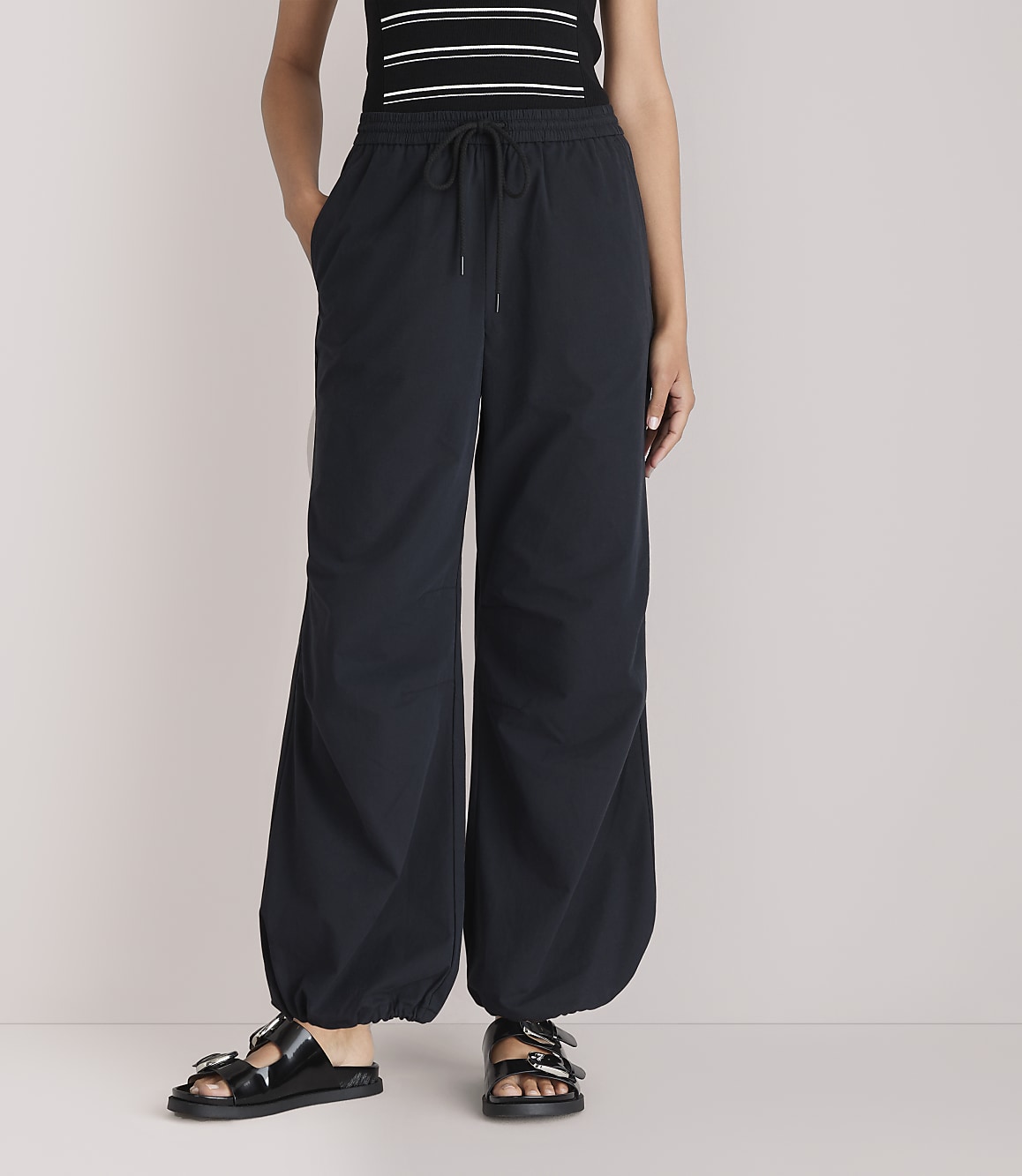 A person stands in black balloon pants and sandals against a plain white background.