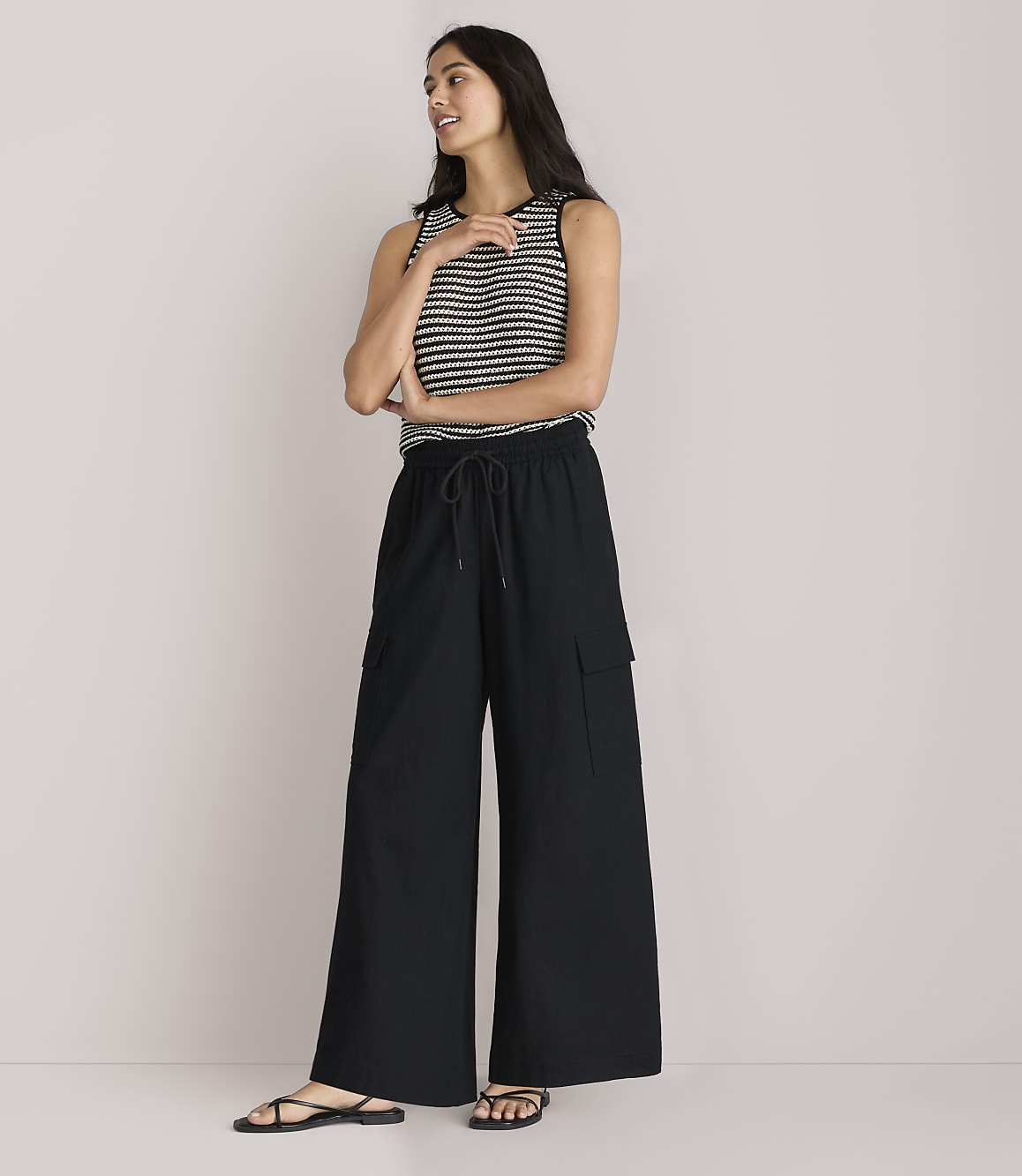 A woman in a striped tank top and black wide-leg pants stands against a plain white background.