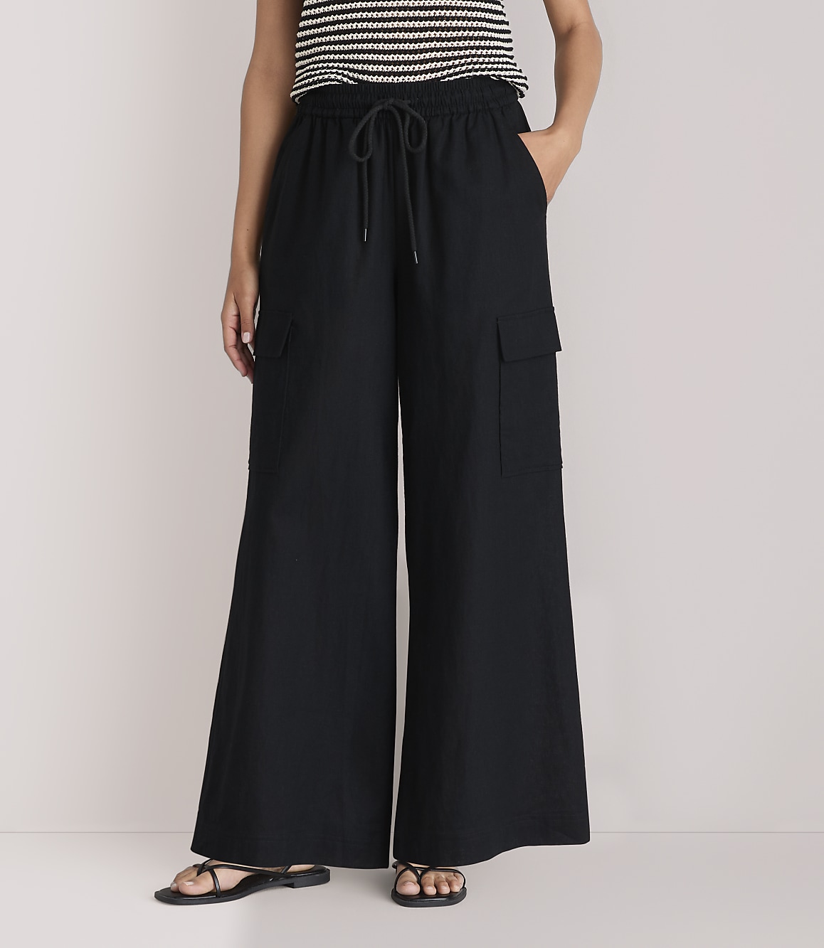 A person wearing black wide-leg cargo pants and a striped top stands against a plain white background.