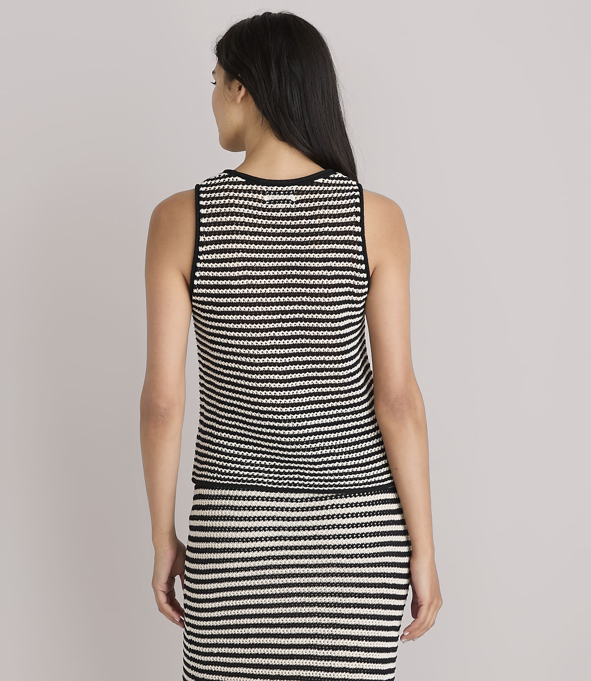 A woman in a striped tank top and skirt stands against a plain white background.