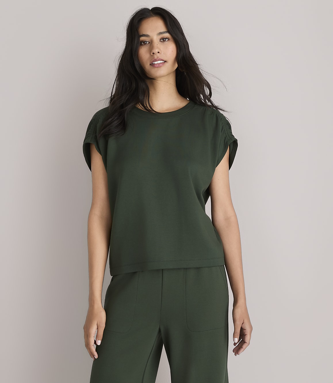 A woman in a dark green top and pants stands against a plain white background.