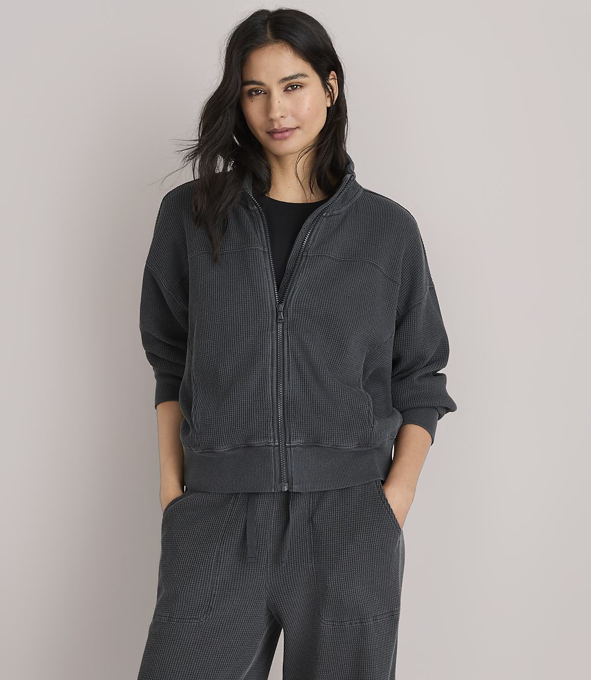 A woman in a dark grey waffle-knit jacket and pants poses against a plain white background.