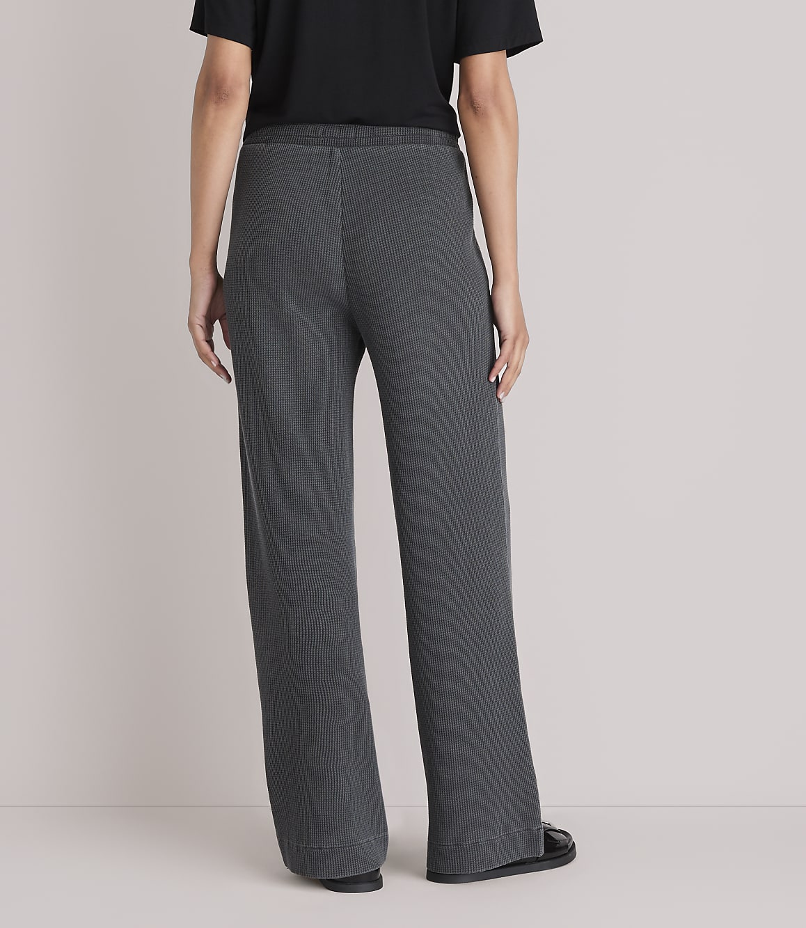A person wearing dark gray wide-leg pants stands against a plain white background.
