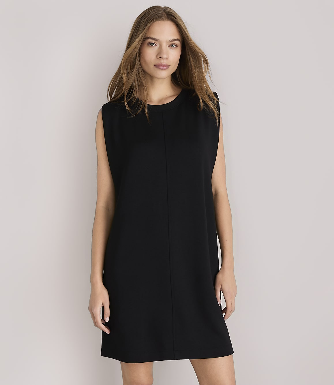 A woman in a black shift dress stands against a plain white background.