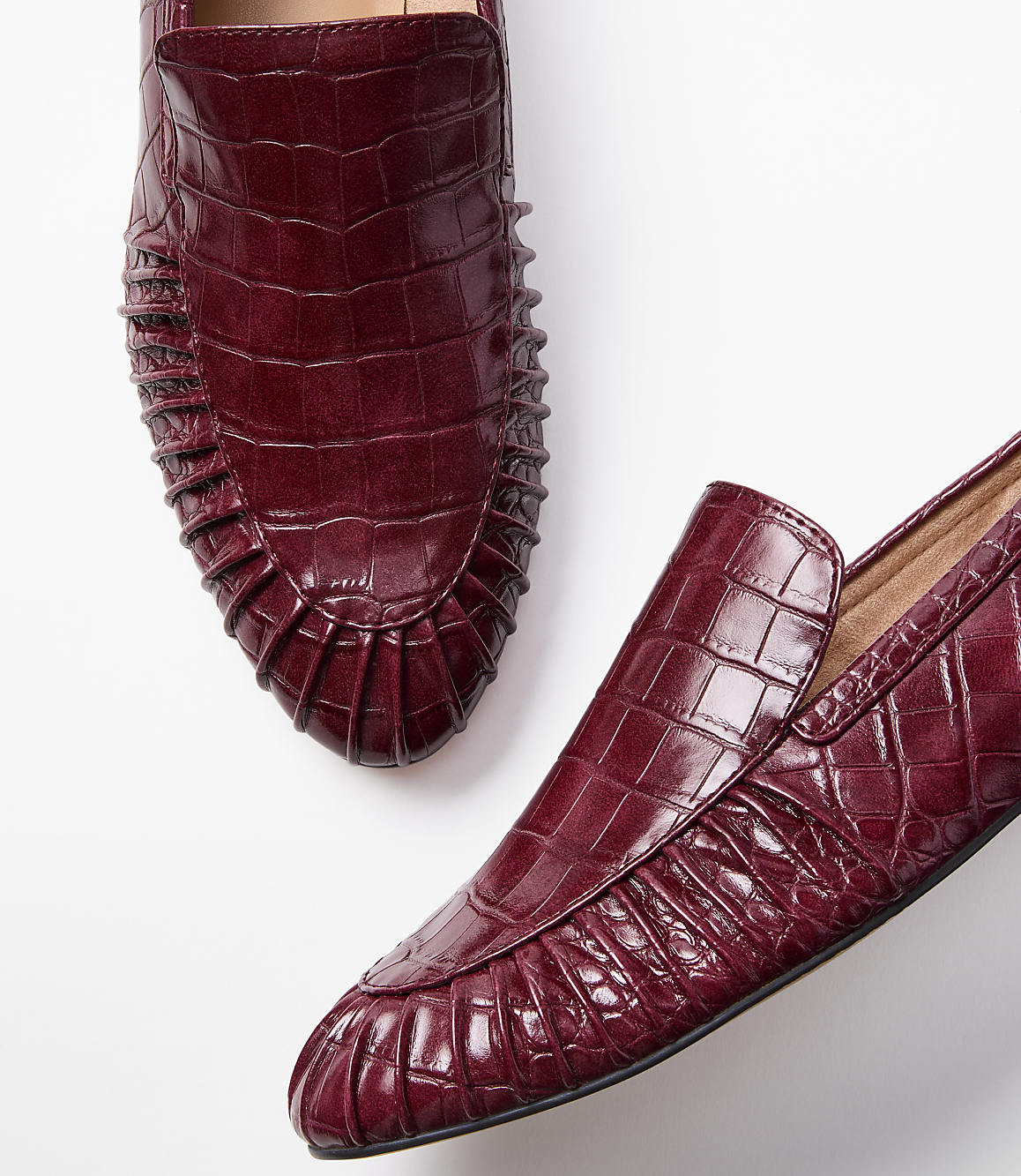 Two burgundy embossed leather loafers with pleated detailing are arranged on a plain white background.