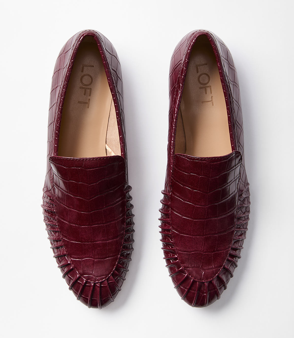 A pair of burgundy embossed loafers with ruffled detailing are laid flat against a plain white background.