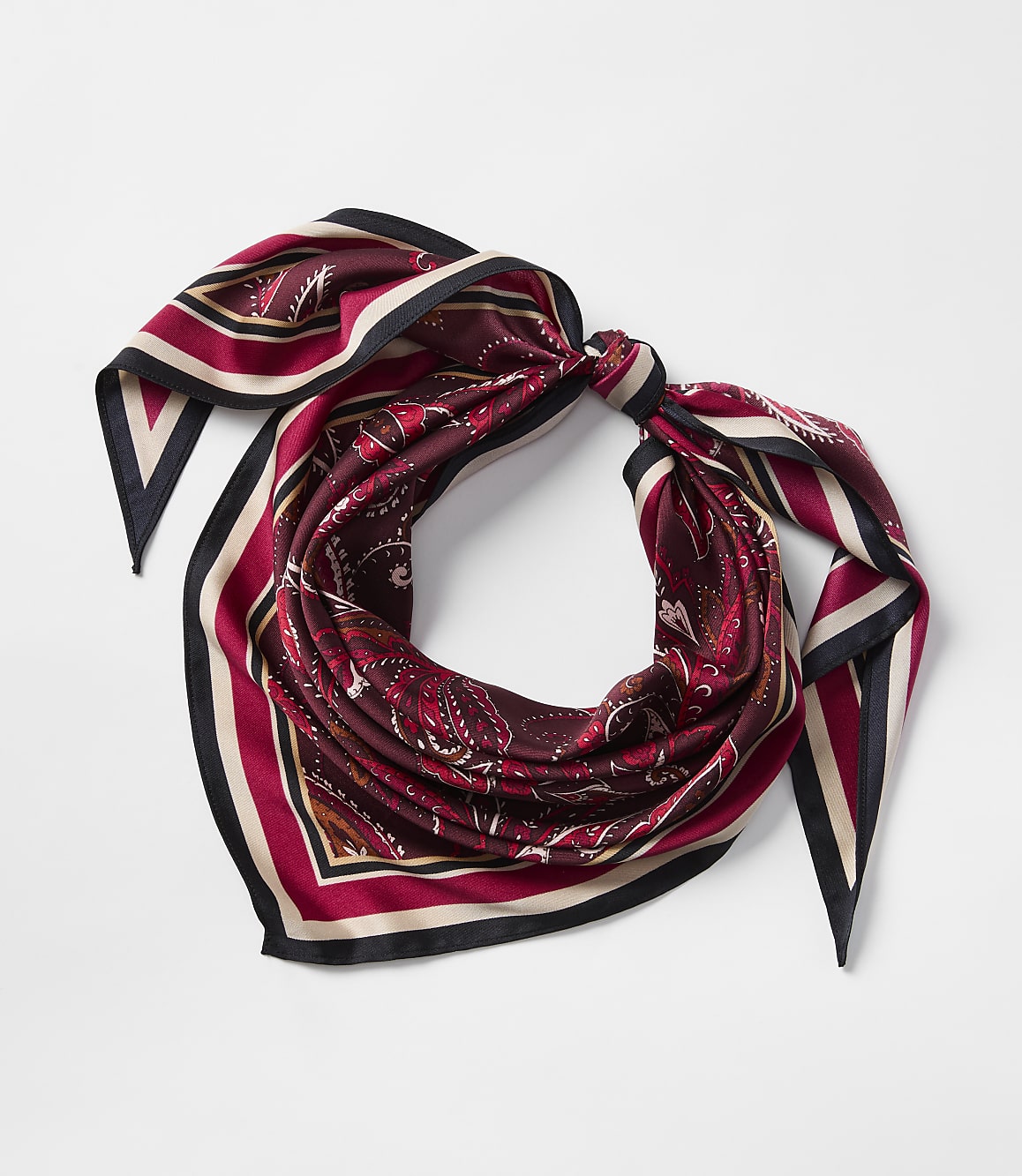 A maroon silk scarf with a paisley pattern and striped border is tied in a knot against a plain white background.