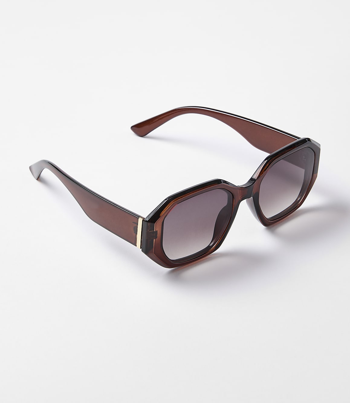 A pair of brown, hexagonal-shaped sunglasses with gradient lenses rests on a plain white background.