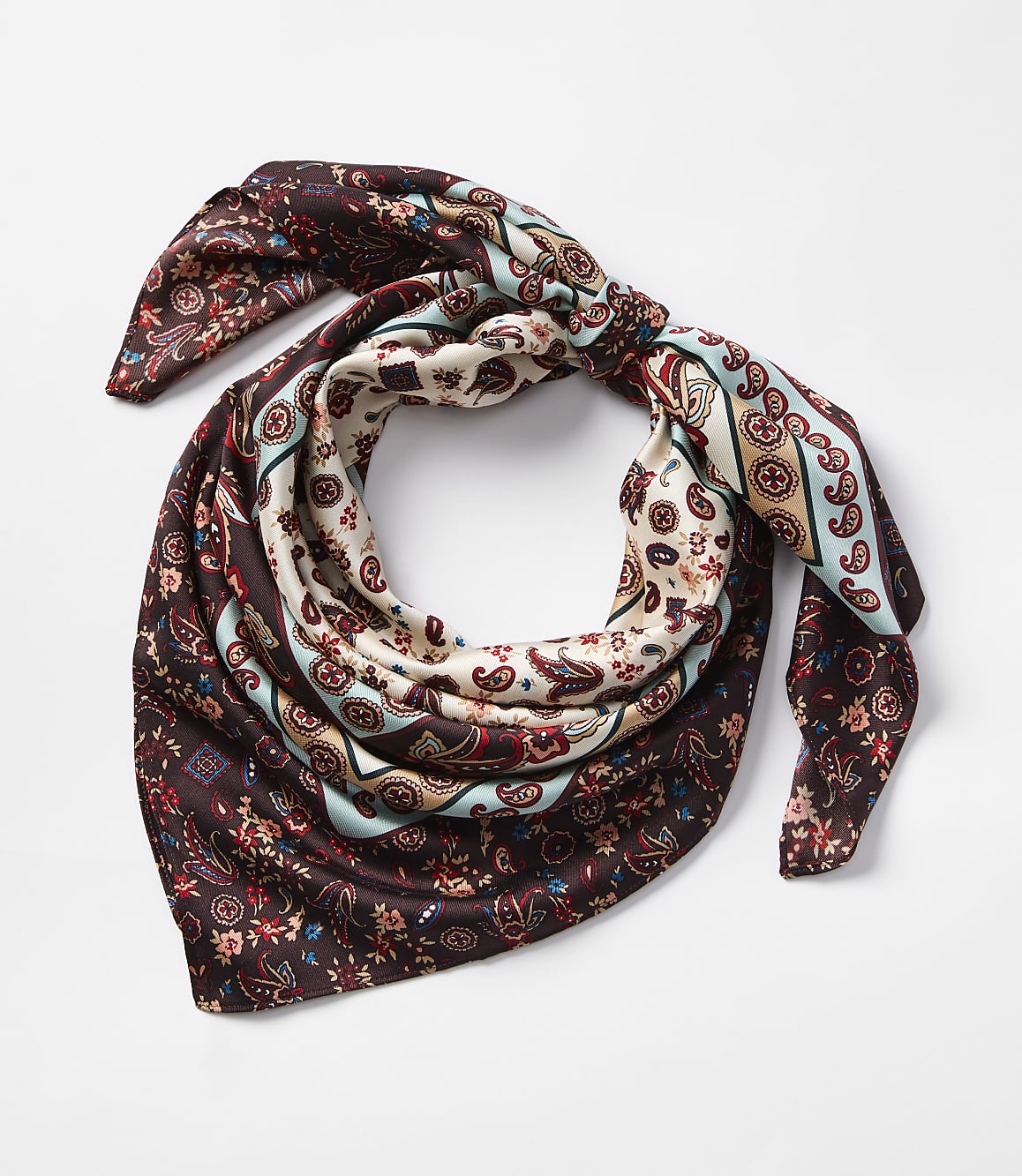 A patterned silk scarf with paisley and floral designs is tied in a knot against a plain white background.