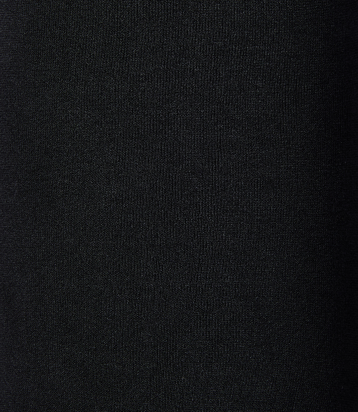 A black, textured fabric fills the frame, with subtle vertical ribbing visible in the foreground and a gradient of darkness towards the right background.