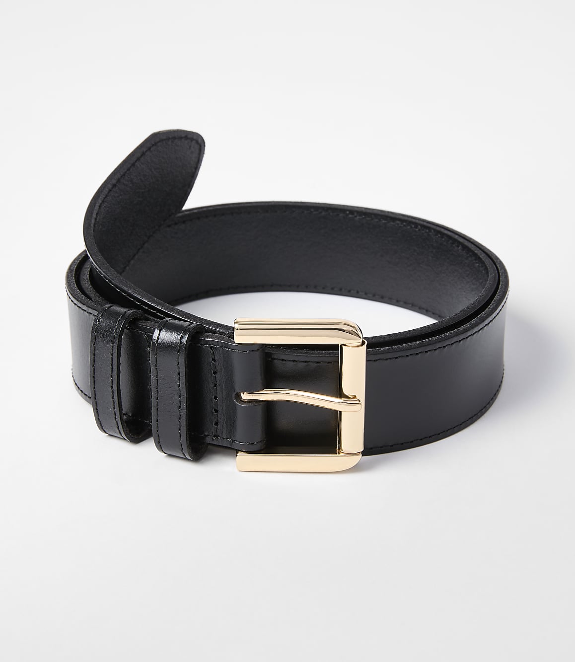 A black leather belt with a gold buckle rests on a white background.