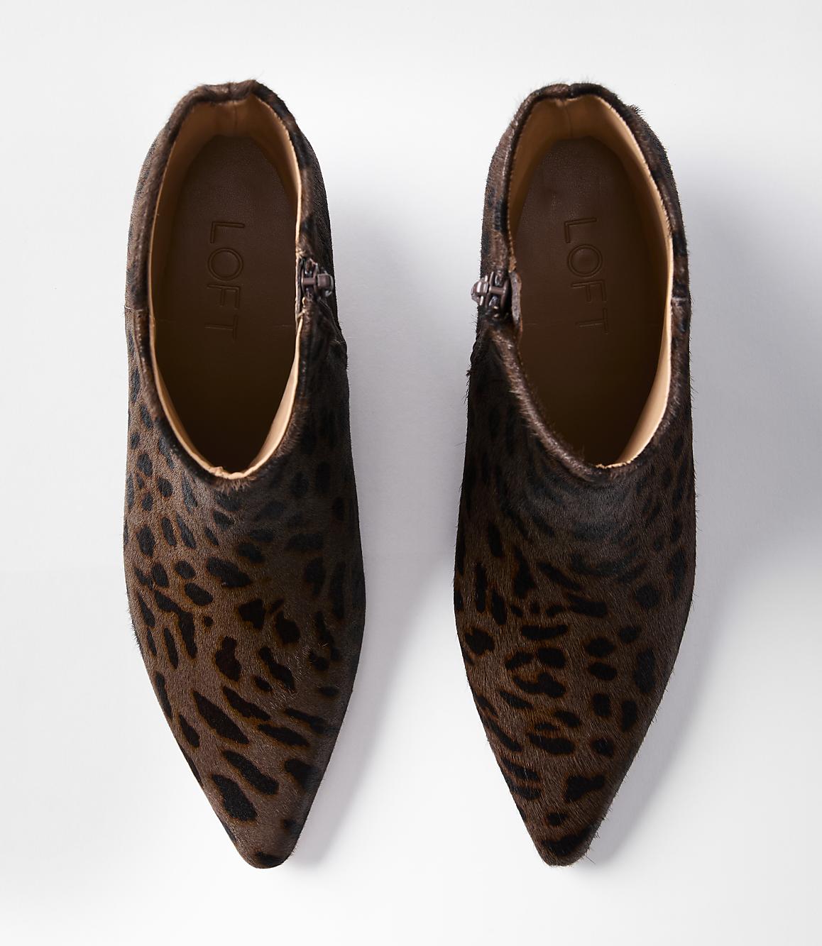 A pair of leopard-print ankle boots with pointed toes are laid out on a white background.