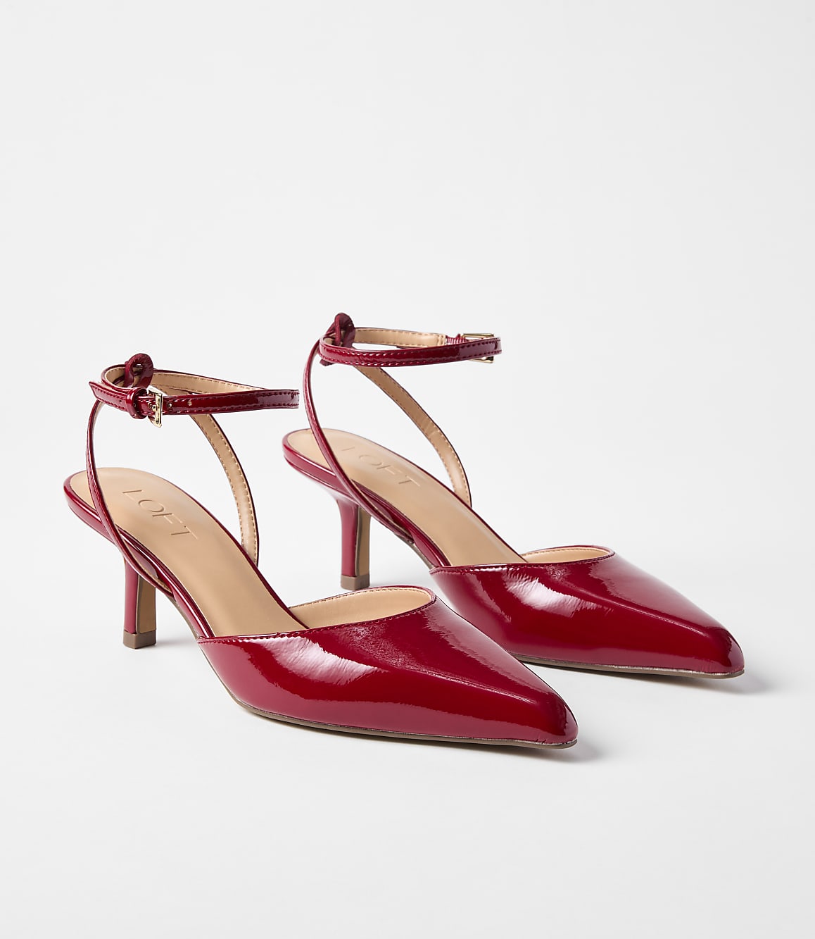 A pair of glossy red patent leather kitten heels with ankle straps rests on a plain white background.