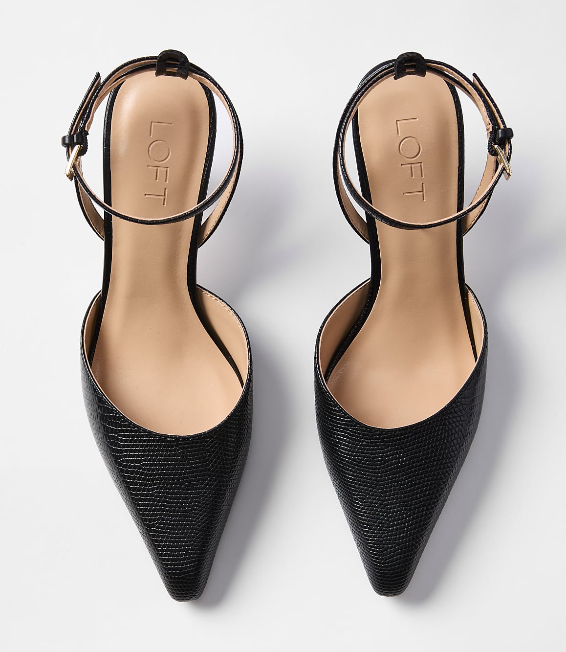 A pair of black, pointed-toe slingback heels with ankle straps rests on a plain white background.