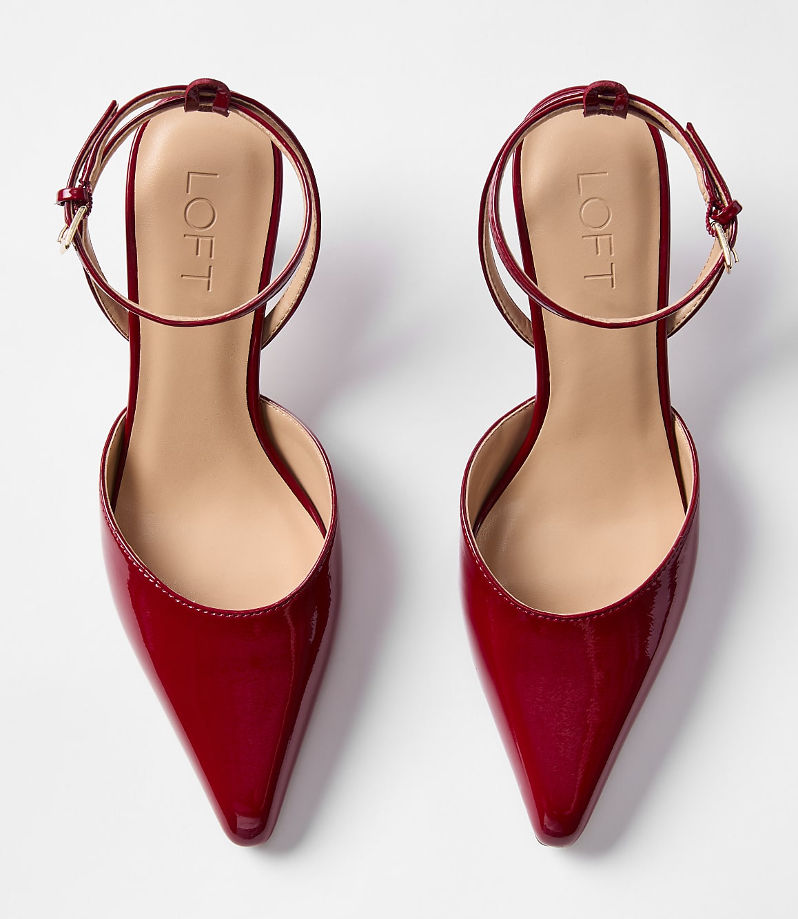 A pair of shiny red pointed-toe flats with ankle straps rests on a plain white background.