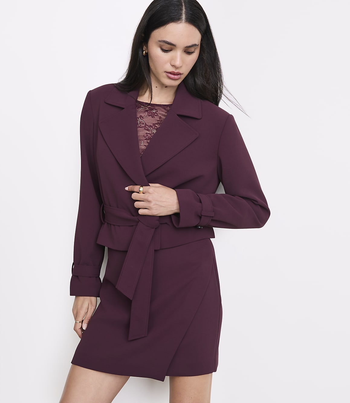 A woman in a burgundy blazer and skirt stands against a plain white background.