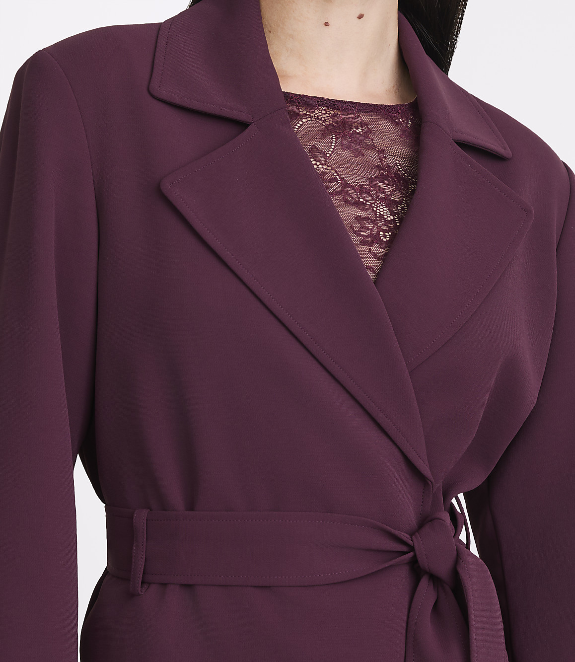 A woman in a plum-colored blazer with a lace top underneath is shown from the chest up.