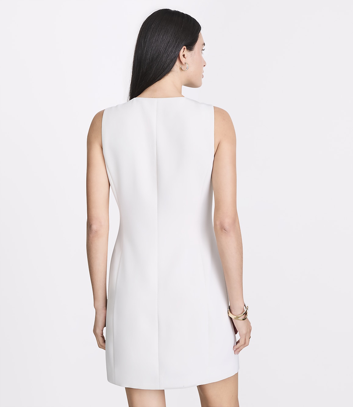 A woman in a white sleeveless dress stands against a plain white background.