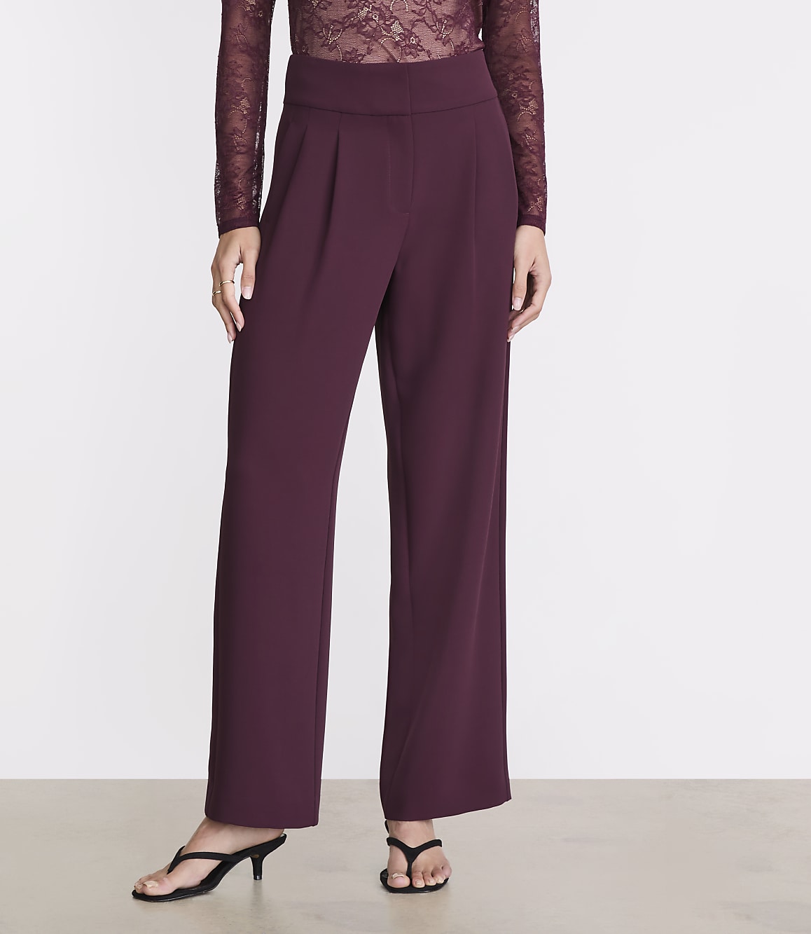 A person in burgundy wide-leg pants and a lace top stands against a plain white background.