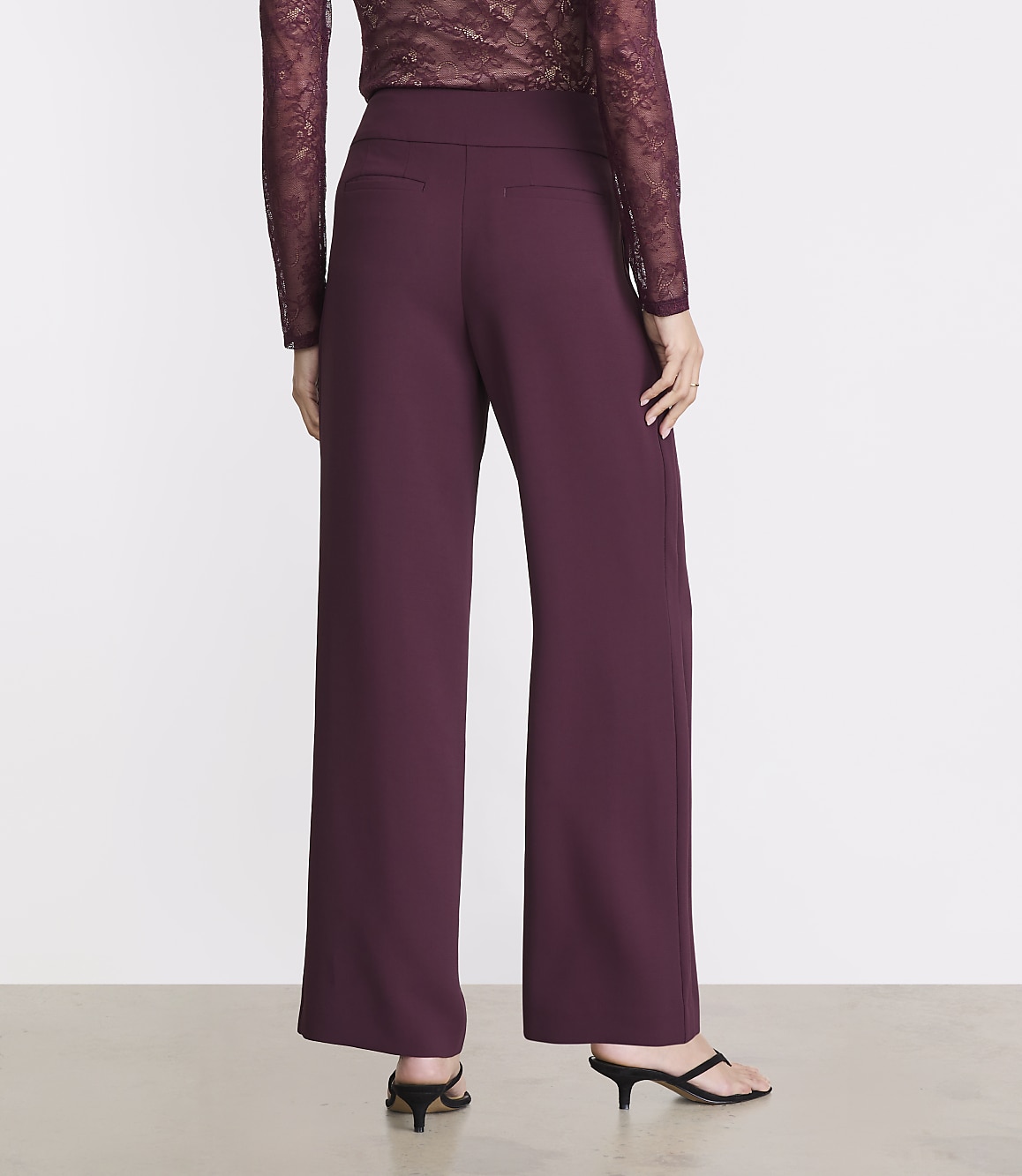 A person wearing burgundy wide-leg pants and a lace top stands against a plain white background.