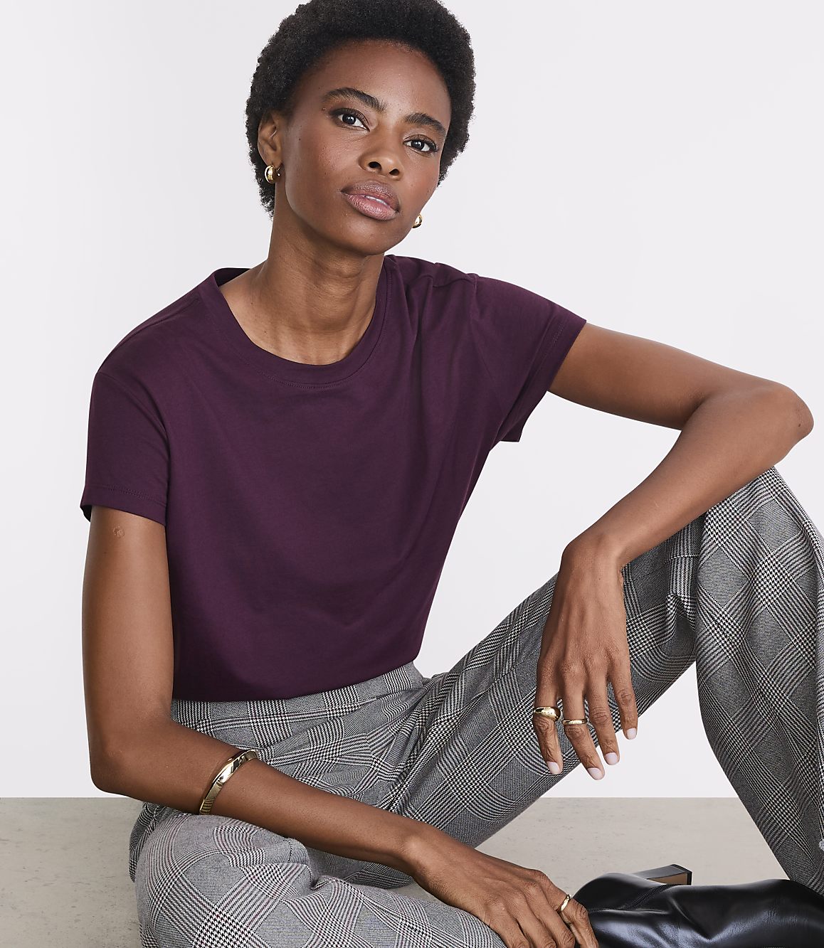 A woman in a plum t-shirt and checkered pants sits against a plain white background.