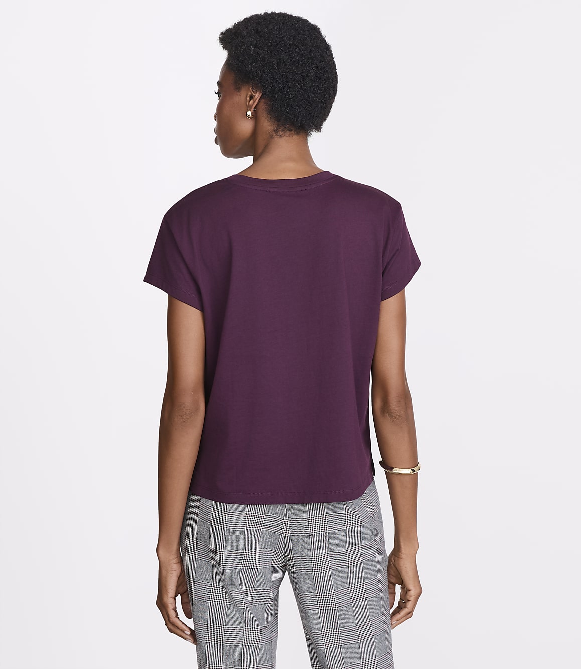A woman in a plum t-shirt and gray checkered pants stands against a plain white background.