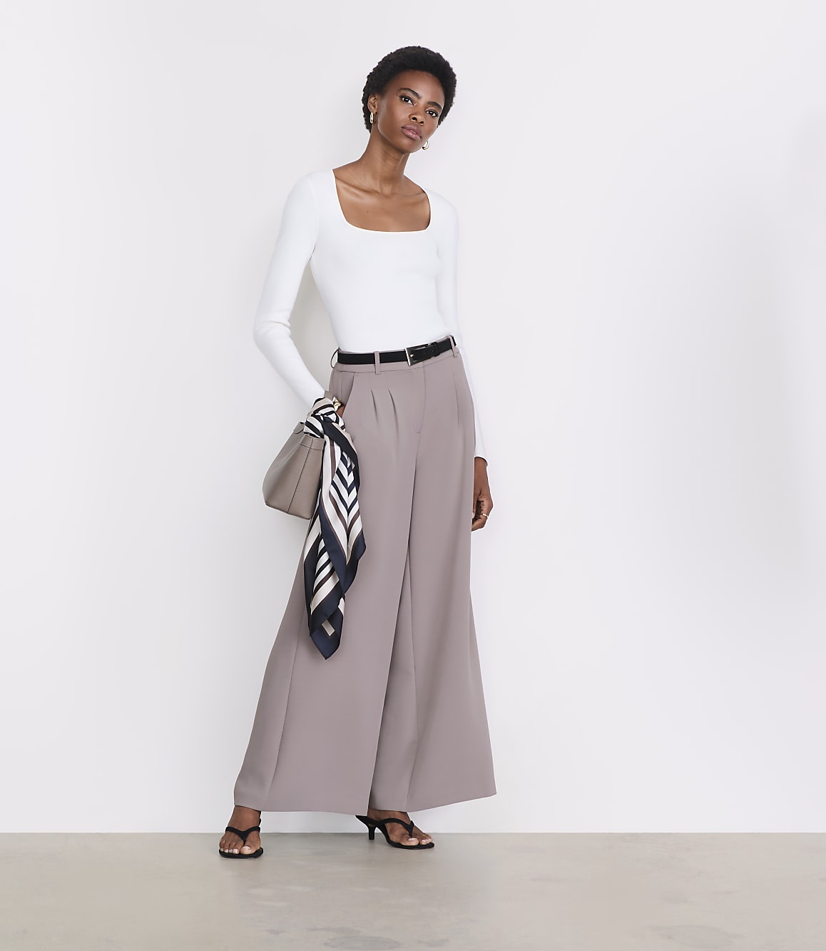 A woman in a white top and wide-leg pants stands against a plain white background.