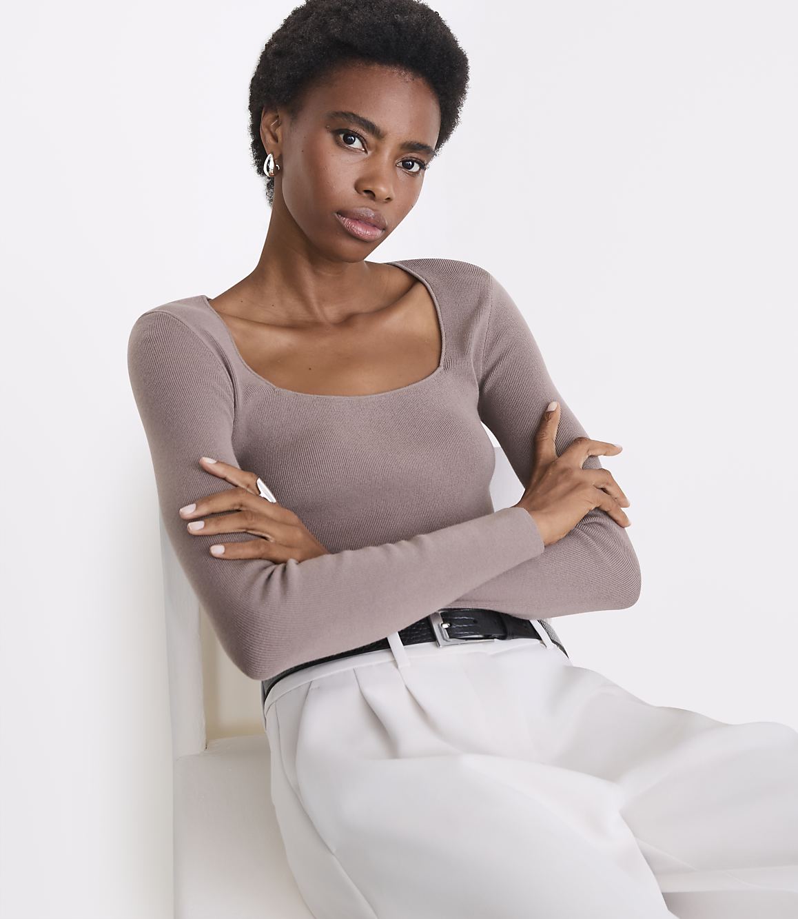 A woman in a taupe ribbed sweater and cream pants poses against a white background.