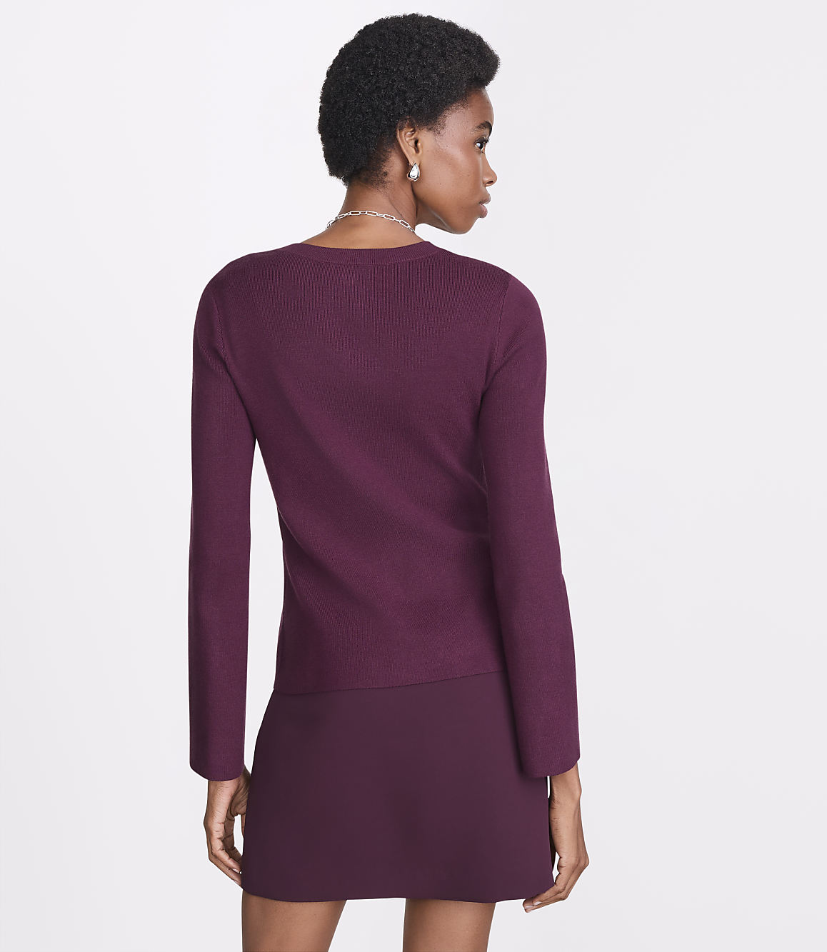 A woman in a burgundy sweater and skirt stands against a plain white background.