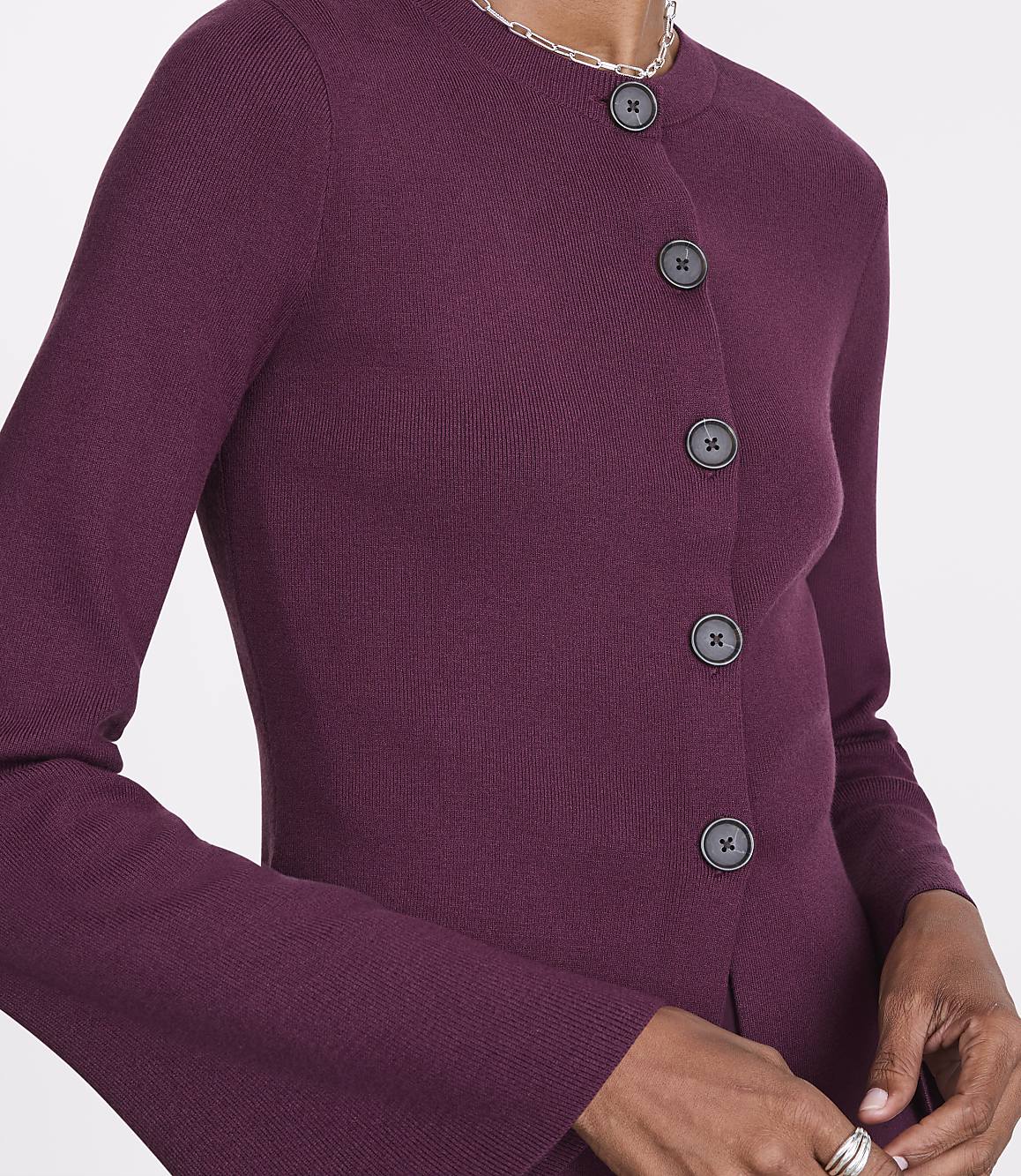 A close-up of a person wearing a plum-colored cardigan with dark buttons is set against a plain white background.