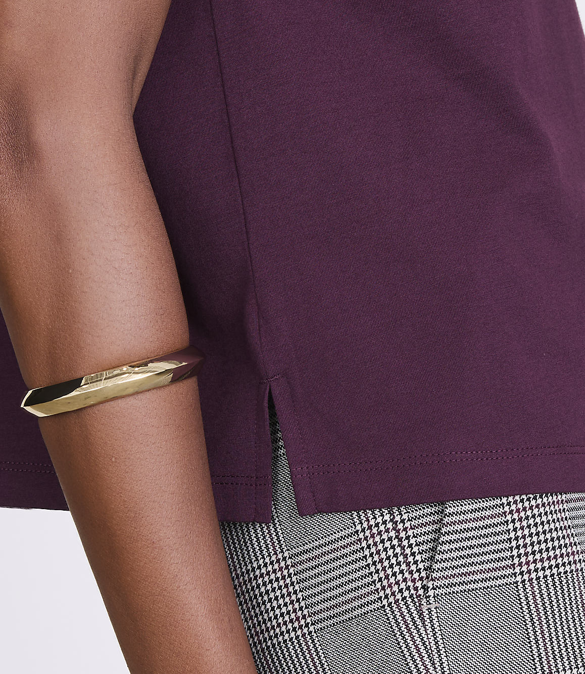 A person's arm wearing a gold bracelet is visible in the foreground, with a plum-colored shirt and plaid pants in the background.