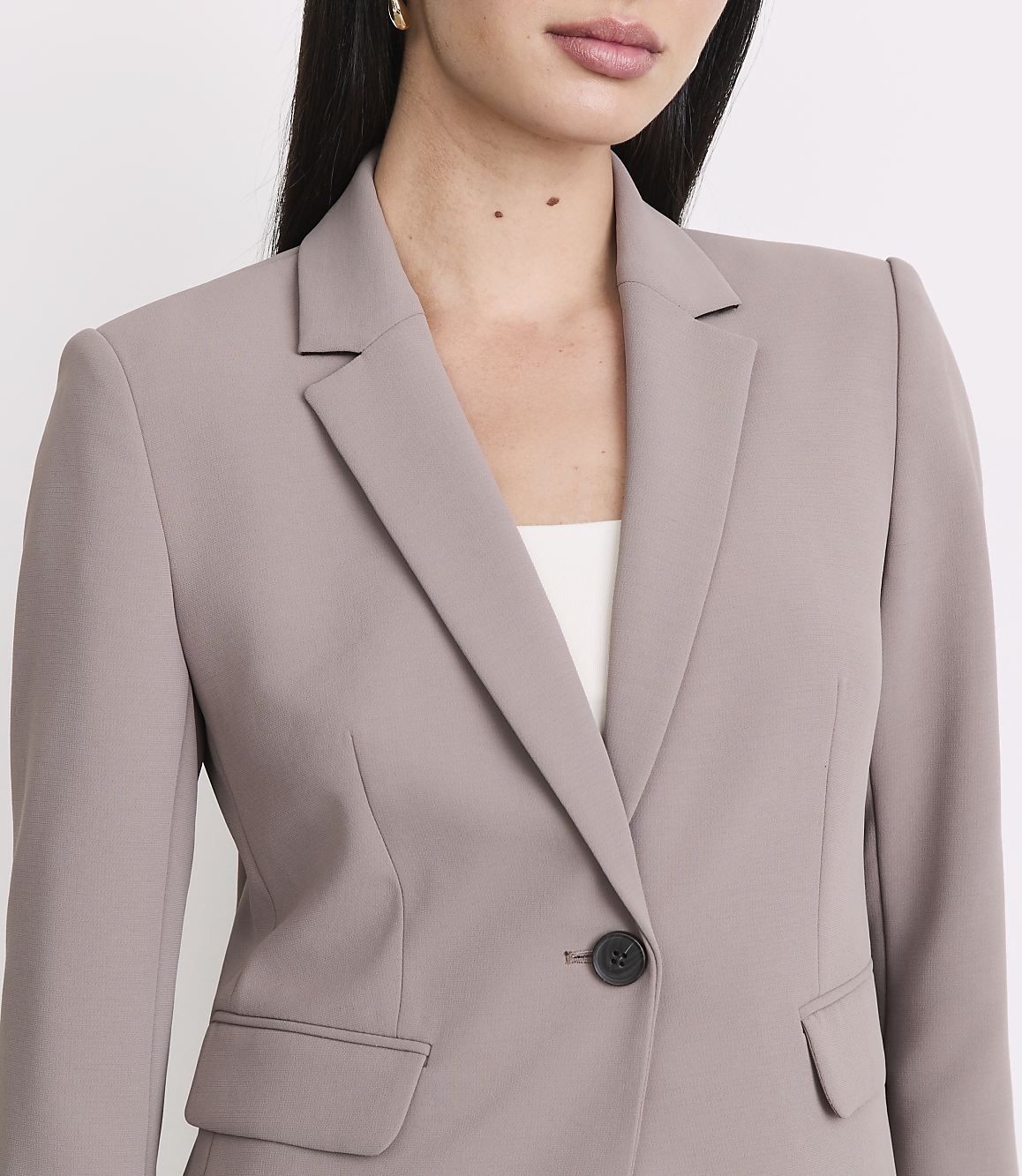 A woman in a taupe blazer stands against a plain white background.