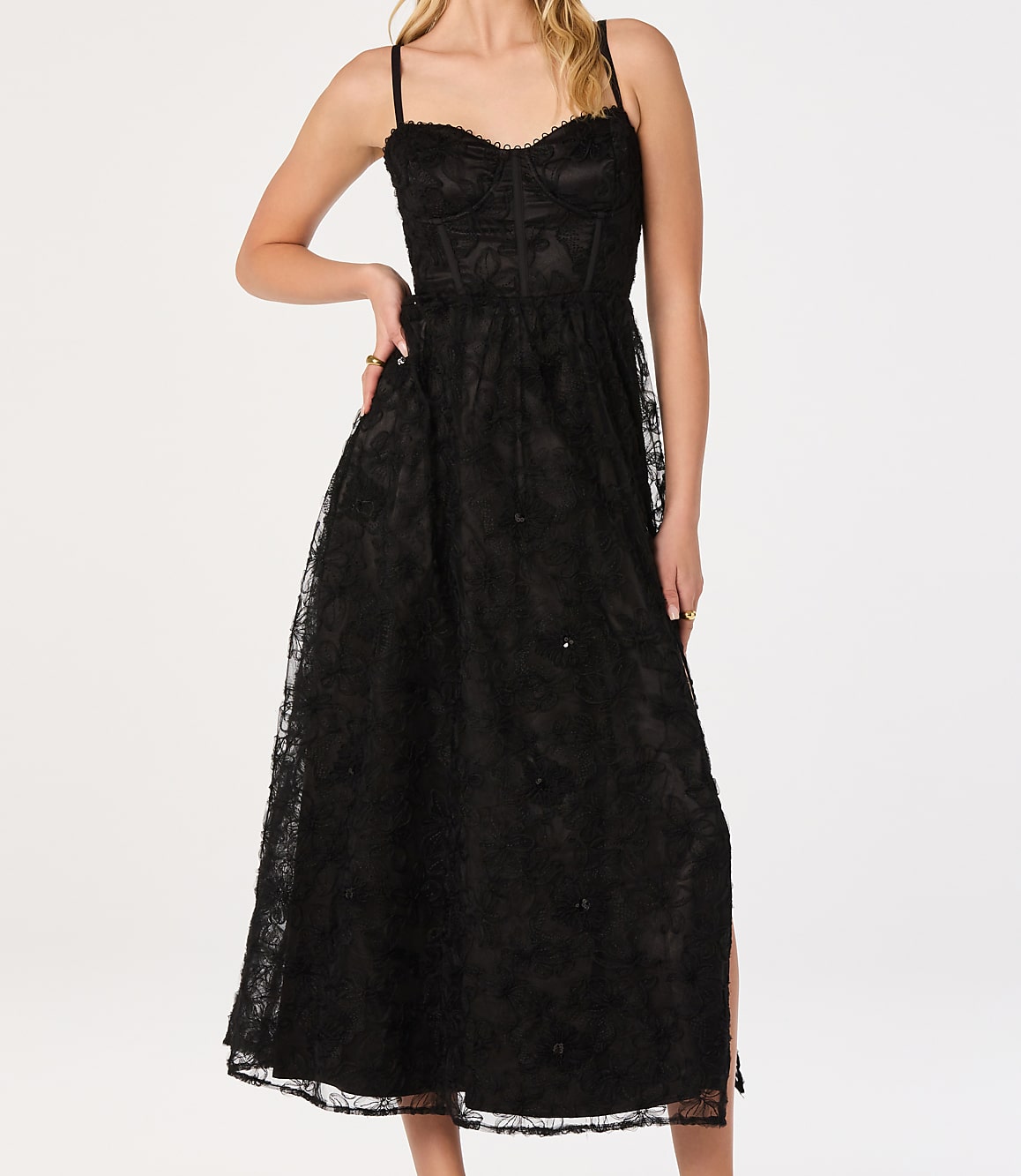 A woman in a black lace dress stands against a plain white background.