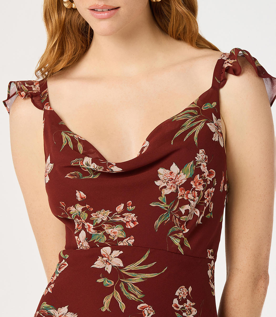 A woman in a floral dress with ruffled sleeves stands against a blurred, light background.