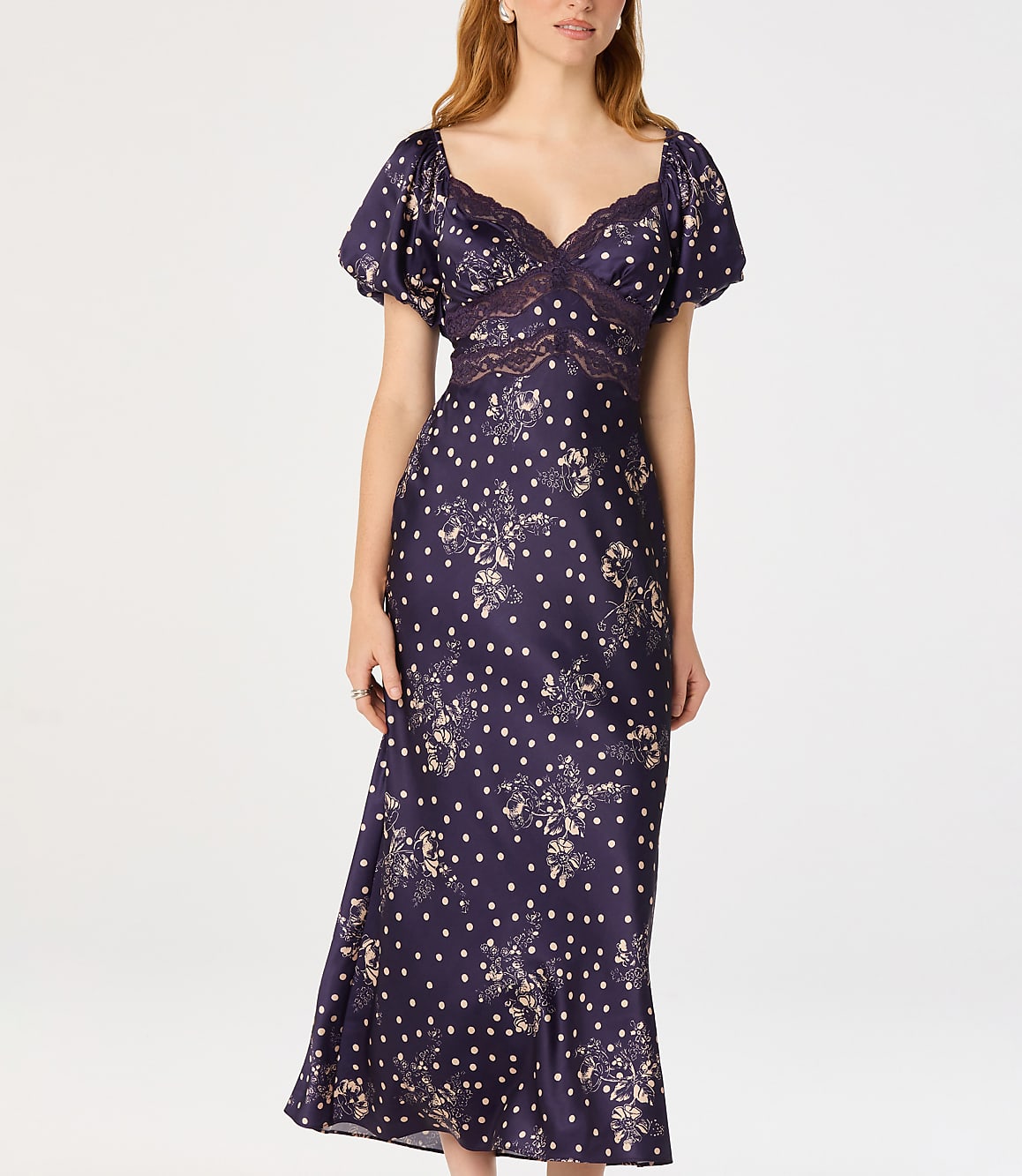 A woman in a dark floral and polka dot dress stands against a plain white background.