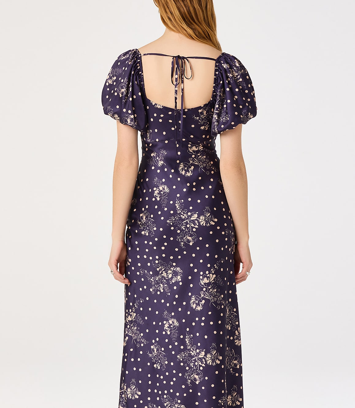 A woman in a dark blue floral and polka dot dress stands against a plain white background.