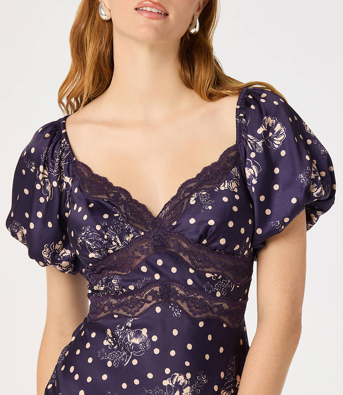 A woman in a dark blue polka dot dress with lace trim is shown against a plain white background.