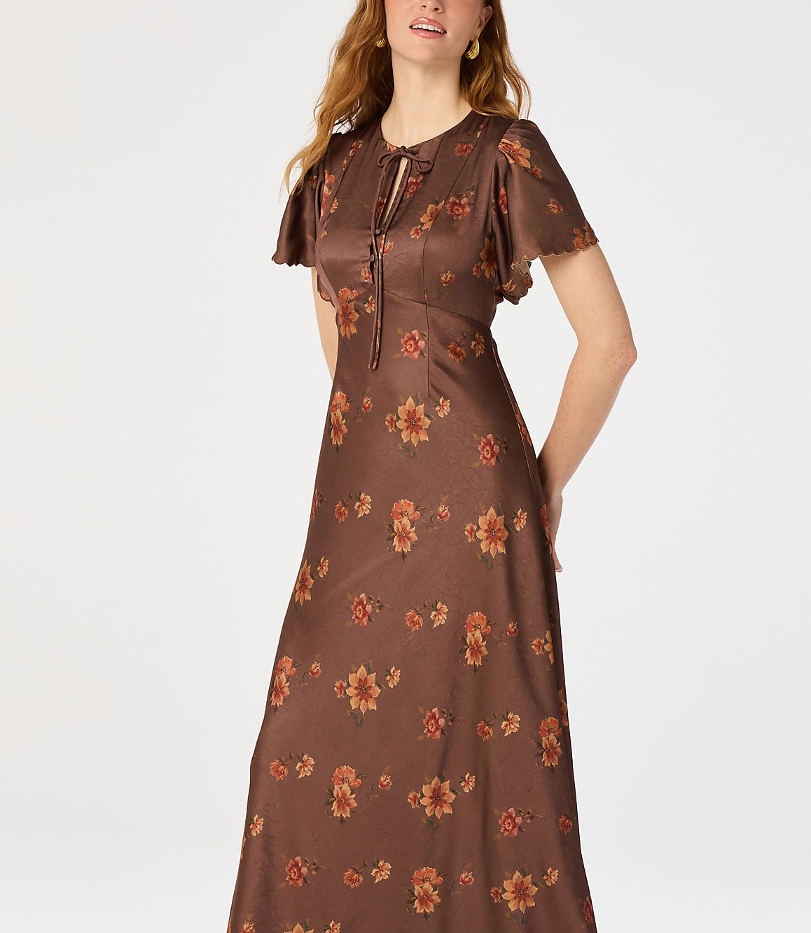 A woman in a brown floral dress stands against a plain white background.